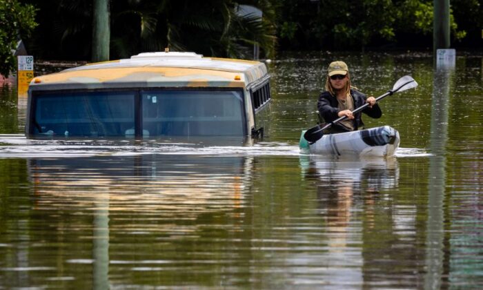 2022 年 2 月 28 日，在澳大利亚布里斯班郊区米尔顿镇一条被淹的街道上，一名男子在一辆被淹的公共汽车旁划着皮划艇。（帕特里克·汉密尔顿/法新社/法新社通过盖蒂图片社）