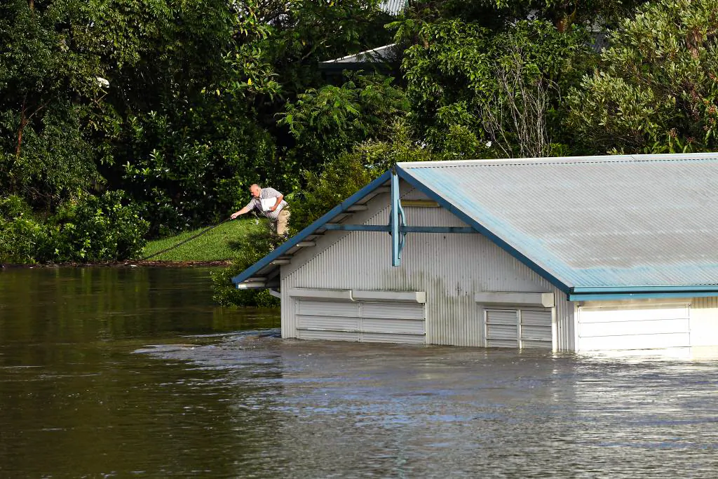 A man pushes away floating debris next to a flooded shed on the bank of over flowing Clarence River in Grafton, Australia, on March 1, 2022. (Saeed Khan/AFP via Getty Images)