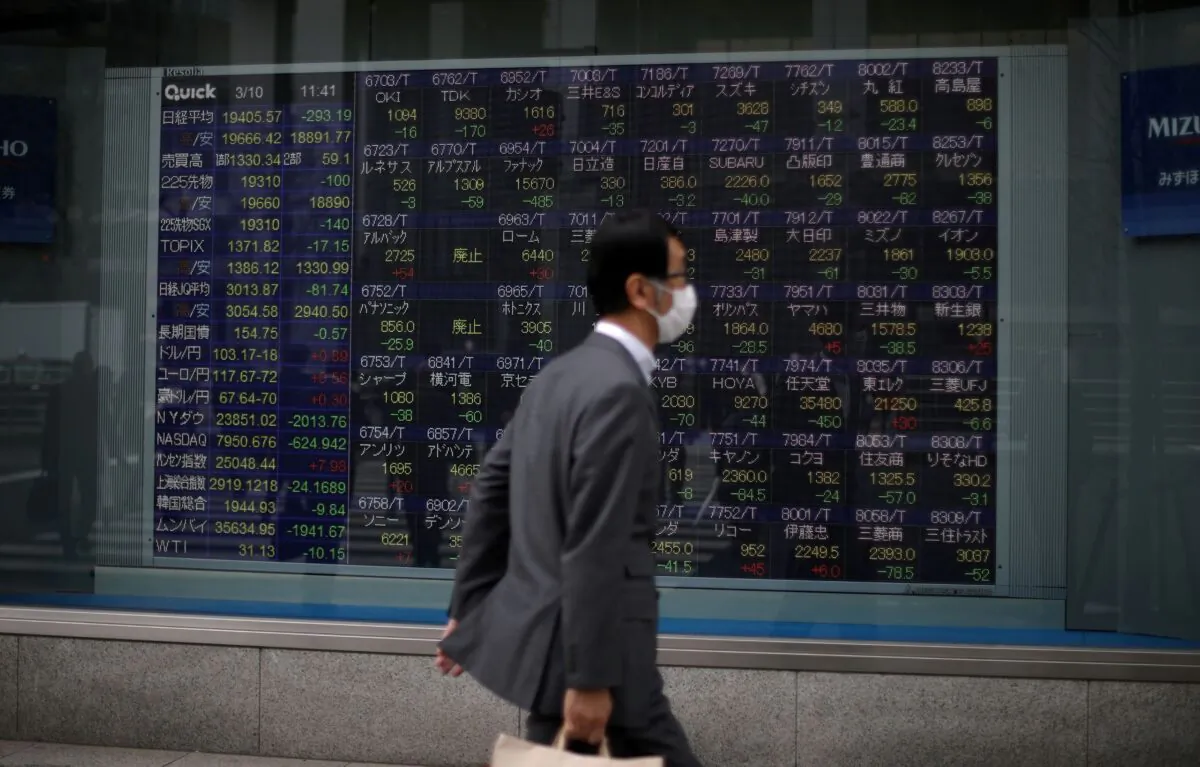 A man wearing a protective face mask walks in front of a stock quotation board outside a brokerage in Tokyo, Japan, on March 10, 2020. (Stoyan Nenov/Reuters)