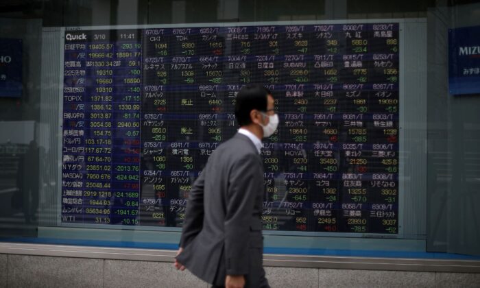 A man wearing a protective face mask walks in front of a stock quotation board outside a brokerage in Tokyo, Japan, on March 10, 2020. (Stoyan Nenov/Reuters)
