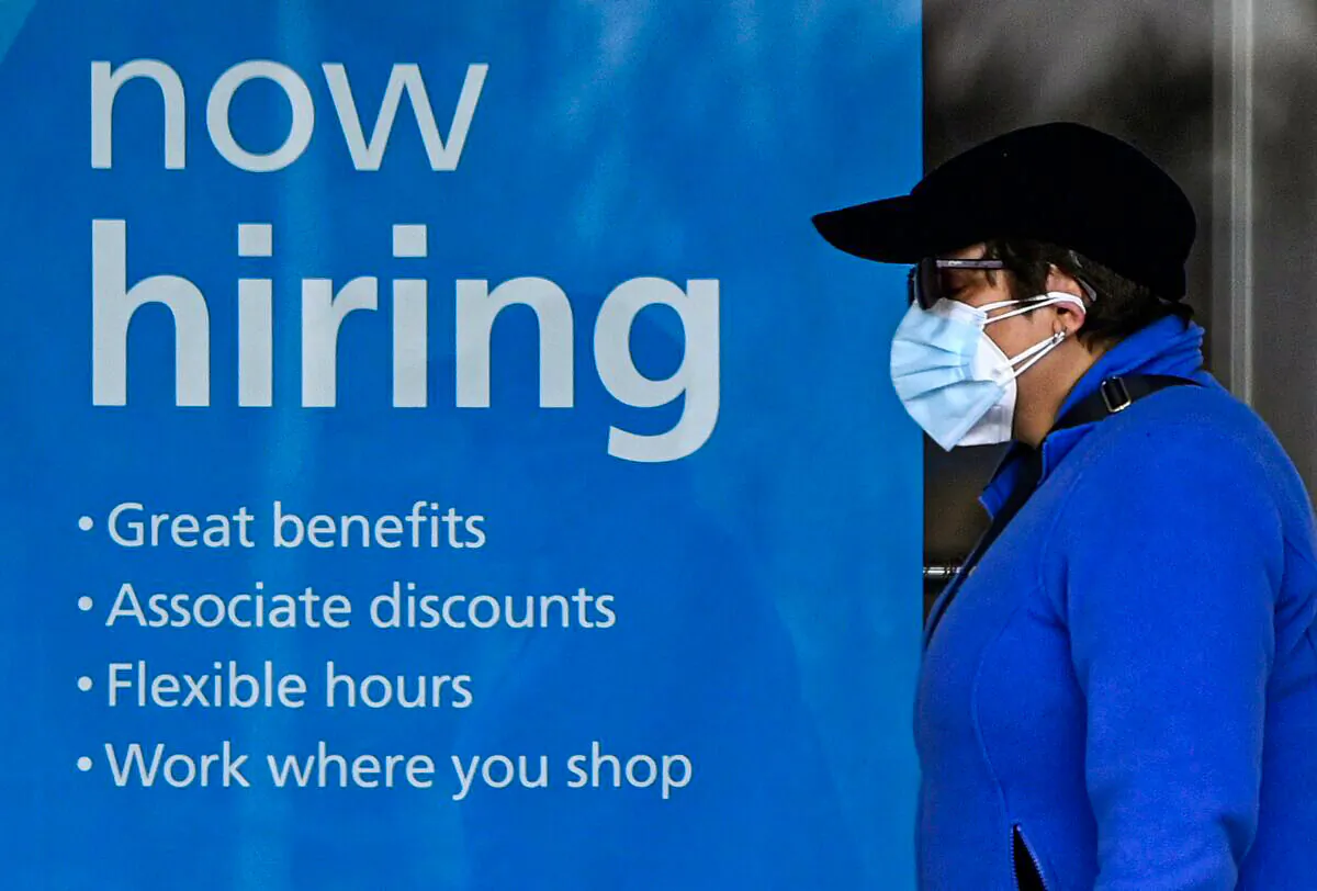 A woman wearing a protective mask walks past a "Now Hiring" sign in front of a store in Arlington, Va., on Jan. 13, 2022. (Olivier Douliery/AFP via Getty Images)