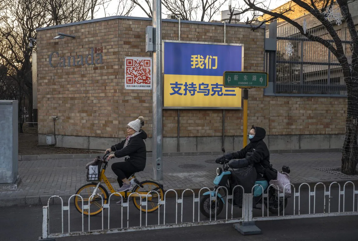 Women ride by a large Ukrainian flag with the slogan "We Support Ukraine" written on it in Chinese characters on the outside wall of the Canadian Embassy in Beijing, China, on March 1, 2022. (Kevin Frayer/Getty Images)