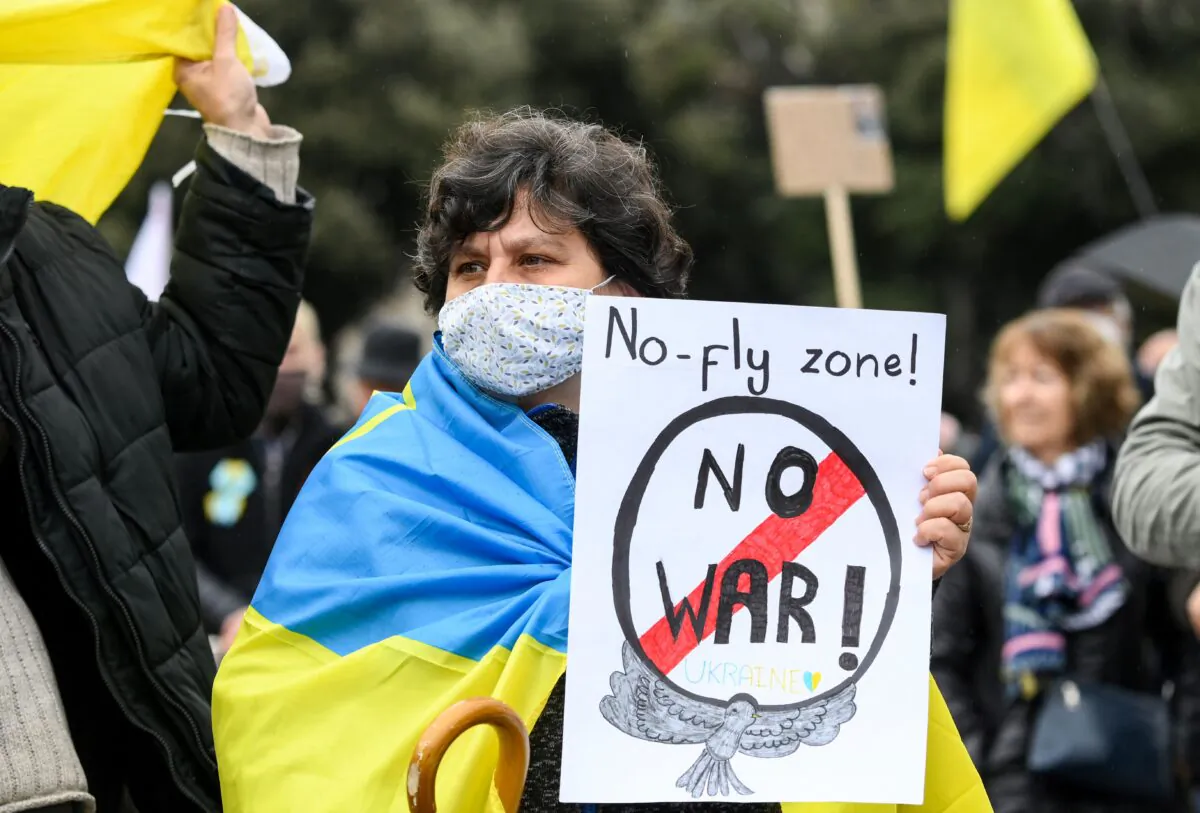 A demonstrator wearing a Ukrainian flag on the shoulders holds a sign reading "No-fly zone! No war!" during a demonstration in support of Ukraine and to protest against Russia's invasion of the country, on the Plaza Catalunya square in Barcelona, on March 6, 2022. (Lluis Gene /AFP via Getty Images)