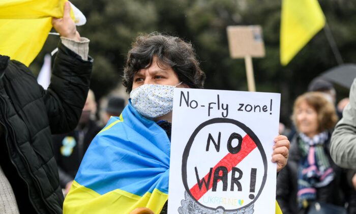A demonstrator wearing a Ukrainian flag on the shoulders holds a sign reading "No-fly zone! No war!" during a demonstration in support of Ukraine and to protest against Russia's invasion of the country, on the Plaza Catalunya square in Barcelona, on March 6, 2022. (Lluis Gene /AFP via Getty Images)
