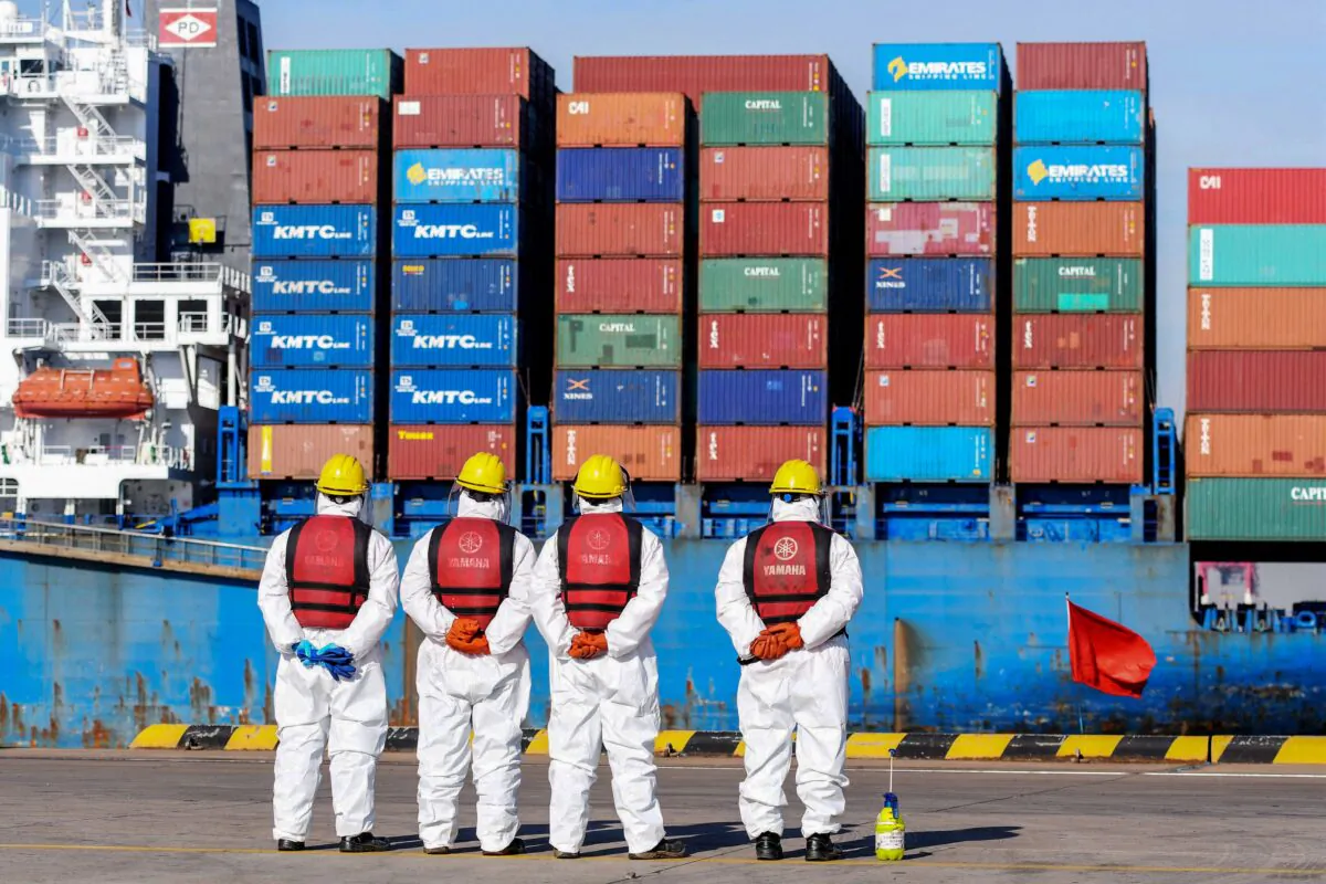 TOPSHOT - Employees wearing personal protective equipment (PPE) look on by a cargo ship at a port in Qingdao in China's eastern Shandong province on January 14, 2022. (STR/AFP via Getty Images)