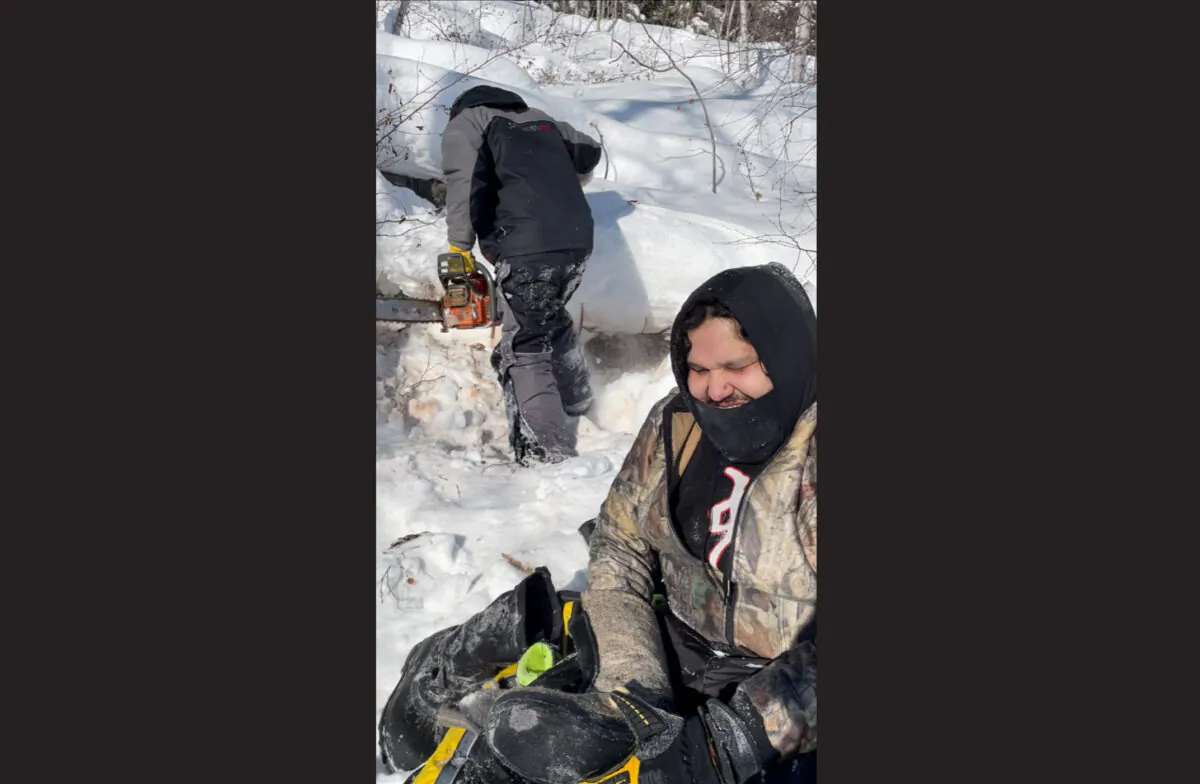 A February 2022 handout photo shows Julian Herman as he dries out his gear and Ron Hyggen preparing to saw wood after their snowmobiles got stuck in slushy snow on Triveet Lake. (The Canadian Press/HO-Thomas Barnett)