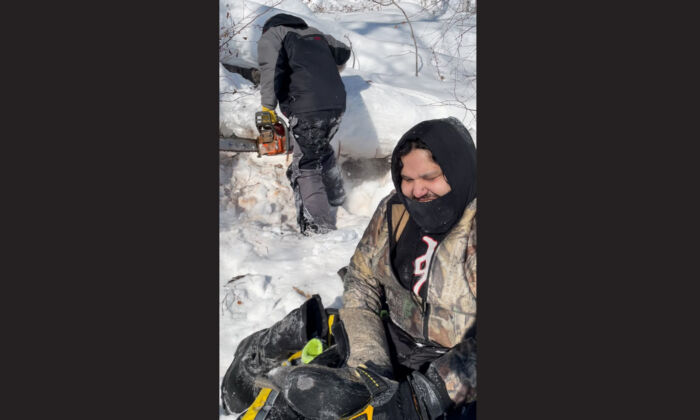 A February 2022 handout photo shows Julian Herman as he dries out his gear and Ron Hyggen preparing to saw wood after their snowmobiles got stuck in slushy snow on Triveet Lake. (The Canadian Press/HO-Thomas Barnett)