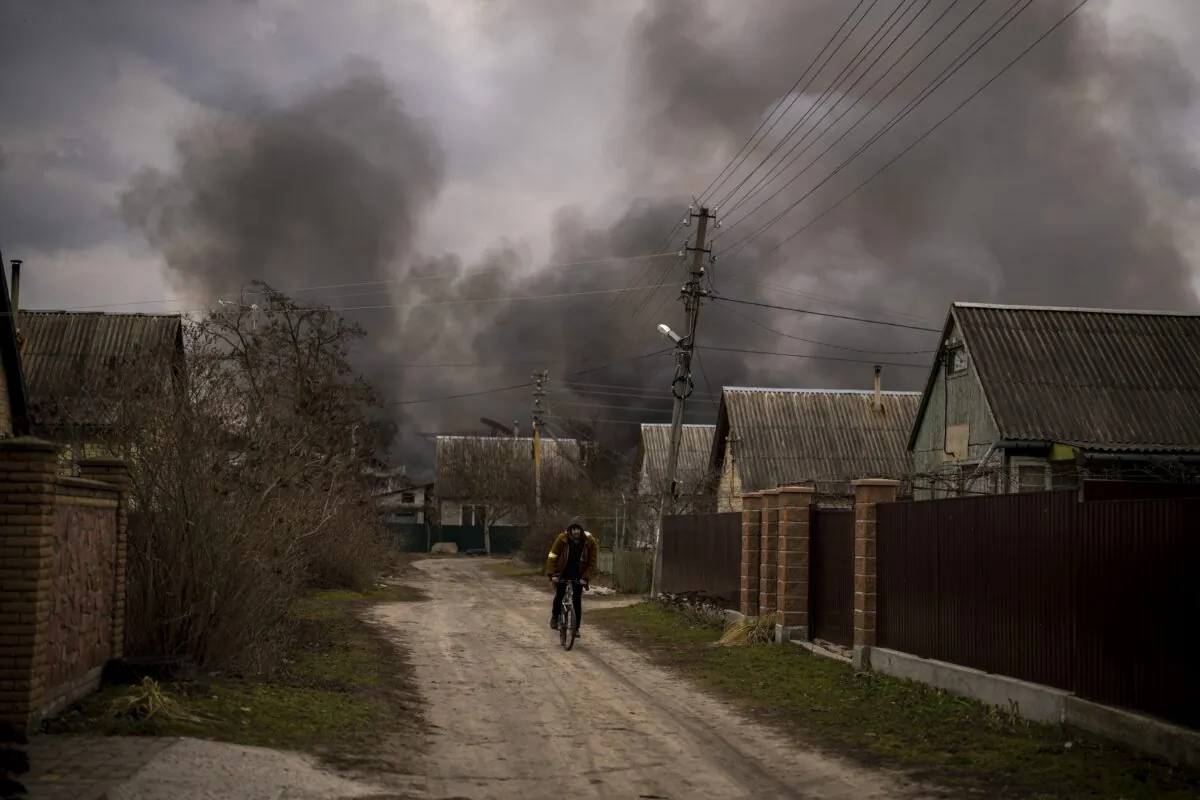 A Ukrainian man rides his bicycle near a factory and a store burning after it was bombarded in Irpin, on the outskirts of Kyiv, Ukraine, on March 6, 2022. (Emilio Morenatti/AP Photo)