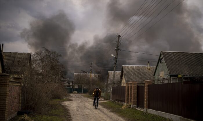 A Ukrainian man rides his bicycle near a factory and a store burning after it was bombarded in Irpin, on the outskirts of Kyiv, Ukraine, on March 6, 2022. (Emilio Morenatti/AP Photo)
