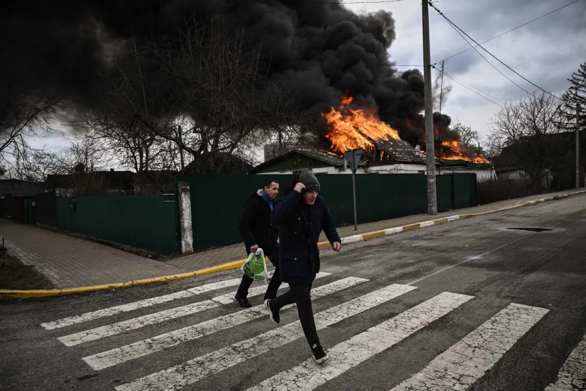 People run for cover in front of a burning house during shelling in the city of Irpin, outside Kyiv, on March 4, 2022. (Aris Messinis/AFP via Getty Images)