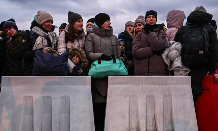 People who fled the war in Ukraine wait in line to board a bus behind removable barriers as police officers and Polish territorial defense soldiers help to manage the crowd after crossing the Polish-Ukrainian border in Medyka, Poland, on March 8, 2022. (Omar Marques/Getty Images)