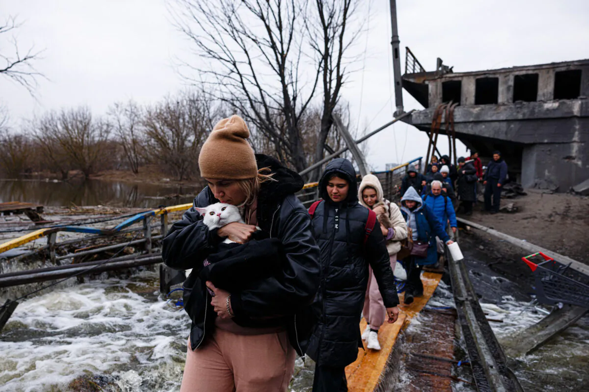 A woman carries her pet cat as evacuees cross a destroyed bridge as they flee the city of Irpin, northwest of Kyiv, Ukraine, on March 7, 2022. (Dimitar Dilkoff/AFP via Getty Images)