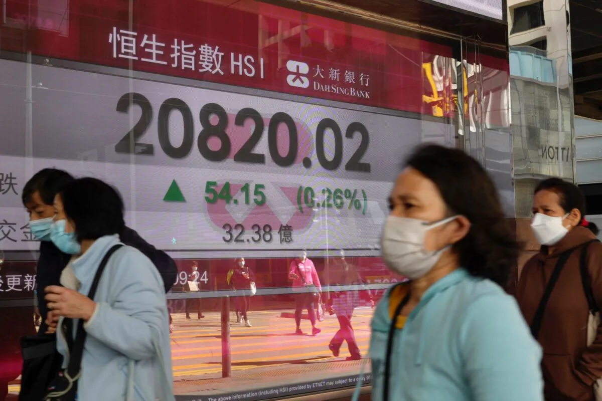 People walk past a bank's electronic board showing the Hong Kong share index at the Hong Kong Stock Exchange on March 9, 2022. (Vincent Yu/AP Photo)