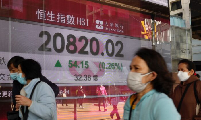 People walk past a bank's electronic board showing the Hong Kong share index at the Hong Kong Stock Exchange on March 9, 2022. (Vincent Yu/AP Photo)