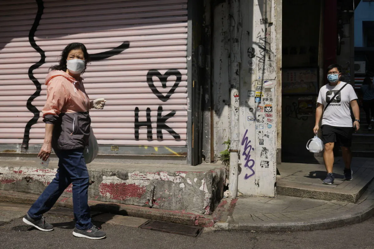 People wearing masks walk across a closed store in Hong Kong, on March 15, 2022. (Kin Cheung/AP Photo)