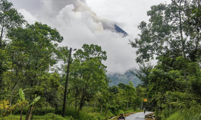 A resident rides a motorcycle past a street with Mount Merapi spewing volcanic materials in the background, seen from Cangkringan village in Sleman, Yogyakarta, on March 10, 2022. (Slamet Riyadi/AP Photo)