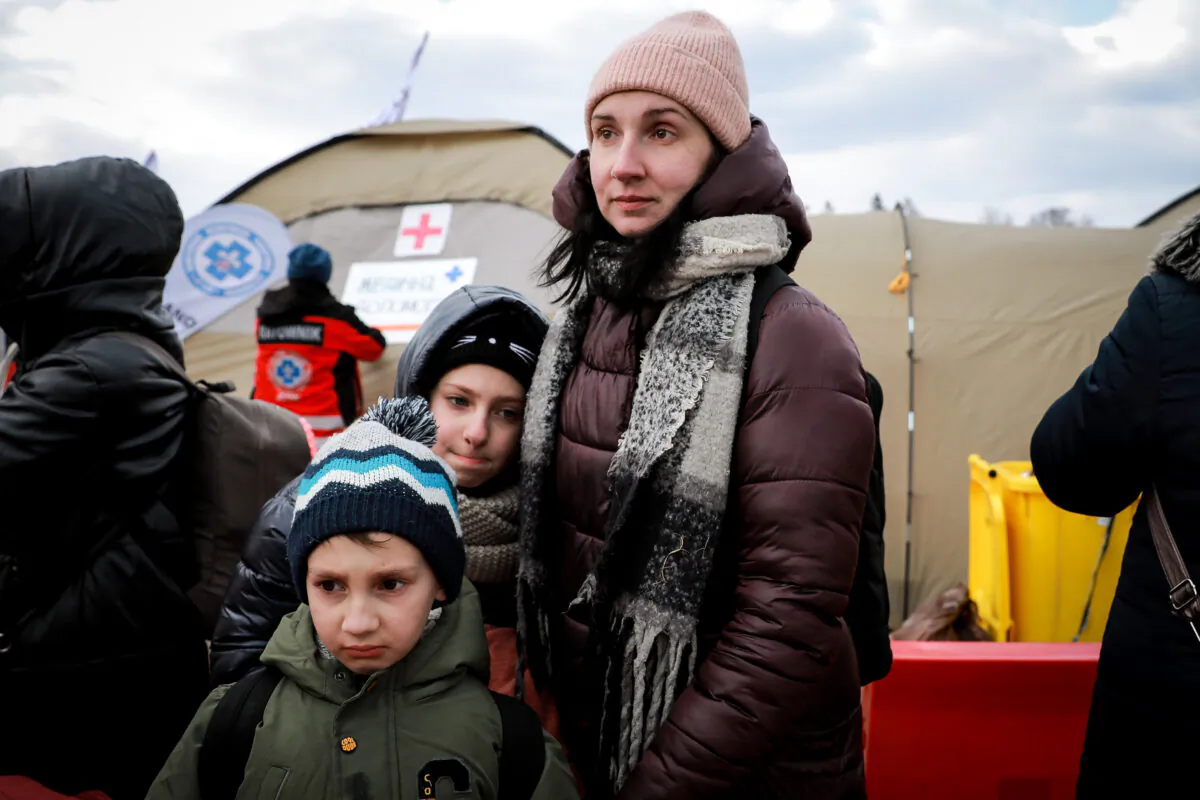 Ukrainian refugees Anna Gorpenich (R) and her children wait for a bus after arriving in Poland through the Medyka border crossing on March 10, 2022. (Charlotte Cuthbertson/The Epoch Times)