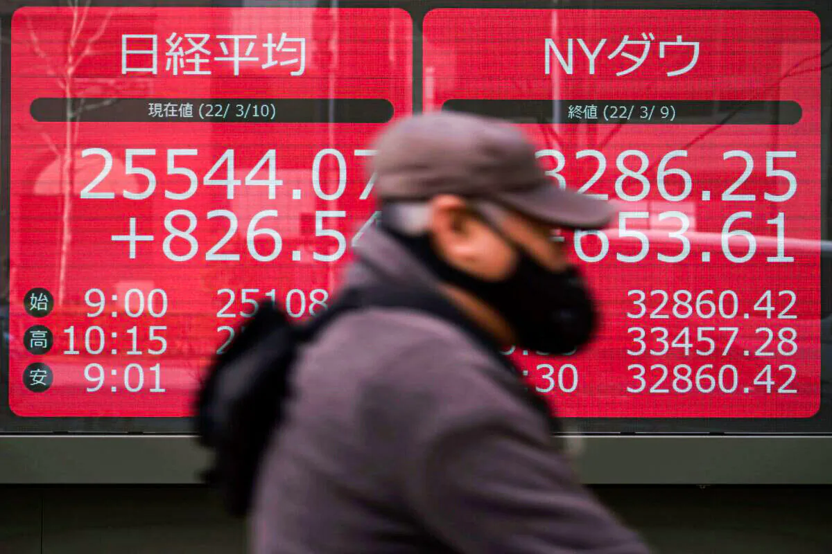 A man wearing a protective mask rides a bicycle in front of an electronic stock board showing Japan's Nikkei 225 and New York Dow indexes at a securities firm in Tokyo, on March 10, 2022. (Eugene Hoshiko/AP Photo)