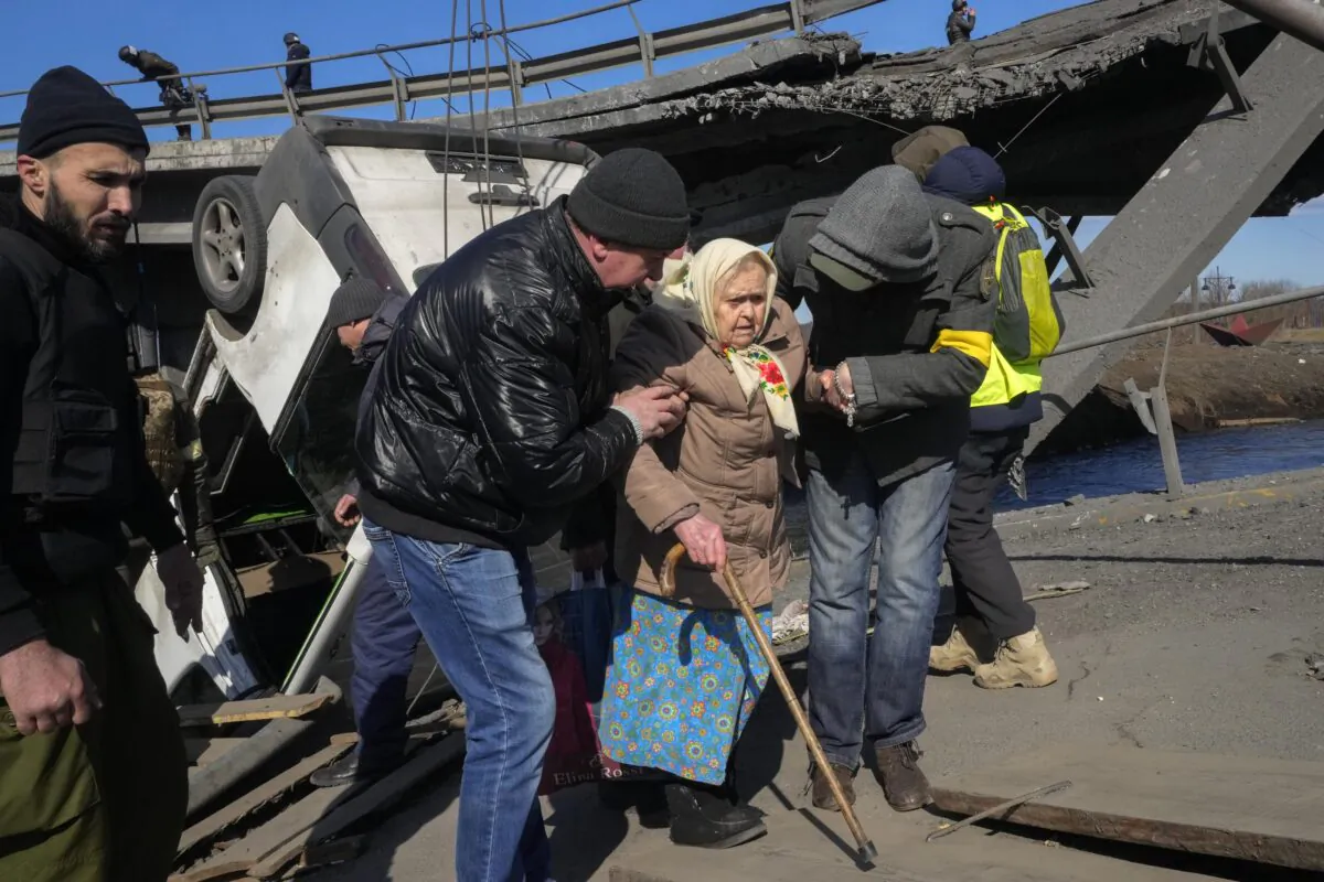 Volunteers pass an improvised path under a destroyed bridge as they evacuate an elderly resident in Irpin, some 16 miles northwest of Kyiv, Ukraine, on March 11, 2022. (Efrem Lukatsky/AP Photo)