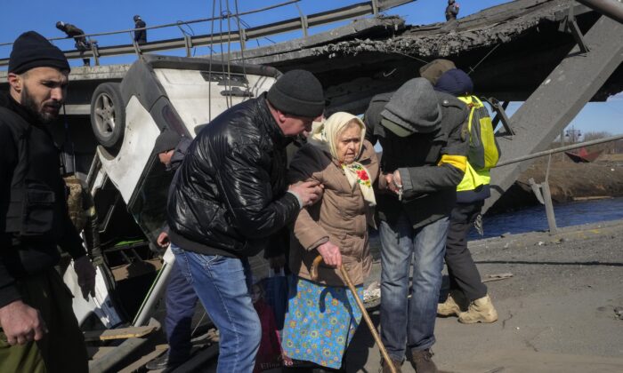 Volunteers pass an improvised path under a destroyed bridge as they evacuate an elderly resident in Irpin, some 16 miles northwest of Kyiv, Ukraine, on March 11, 2022. (Efrem Lukatsky/AP Photo)