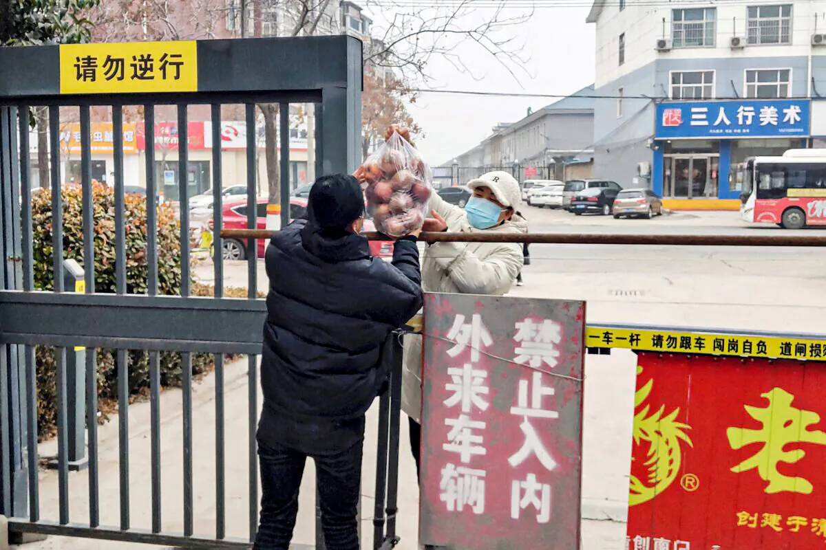 A resident receives food at the entrance of a residental area closed off and restricted due to an outbreak of the Covid-19 coronavirus in Anyang in China's central Henan Province on Jan. 12, 2022. (STR/AFP via Getty Images)