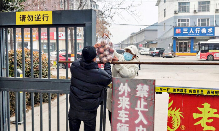 A resident receives food at the entrance of a residental area closed off and restricted due to an outbreak of the Covid-19 coronavirus in Anyang in China's central Henan Province on Jan. 12, 2022. (STR/AFP via Getty Images)