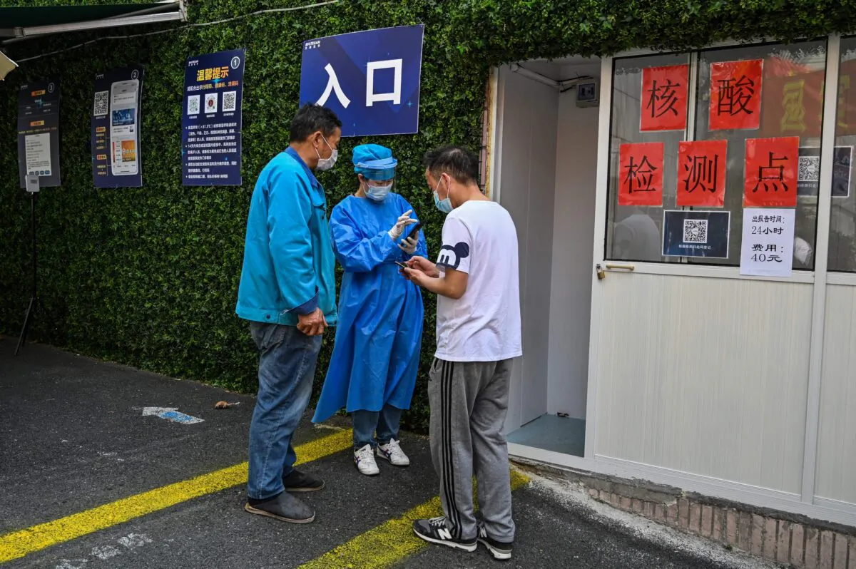 A health worker (C) helps people to fill the information requested in an app to obtain a code and be able to be tested as a measure against the COVID-19 coronavirus near the Shanghai Jin'an Central Hospital, in Shanghai on March 14, 2022. (Hector Retamal/AFP via Getty Images)