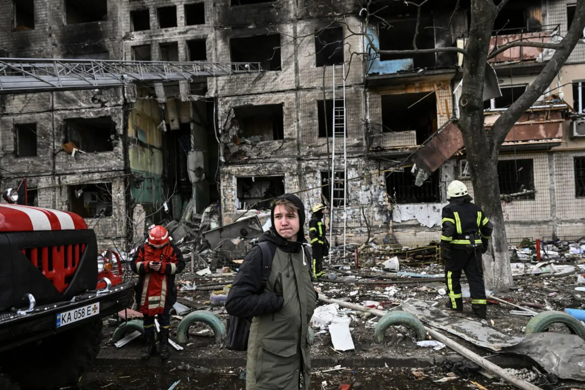 A citizen stands near firefighters in front of a destroyed apartment building after it was shelled in the northwestern Obolon district of Kyiv, Ukraine, on March 14, 2022. (Aris Messinis/AFP via Getty Images)
