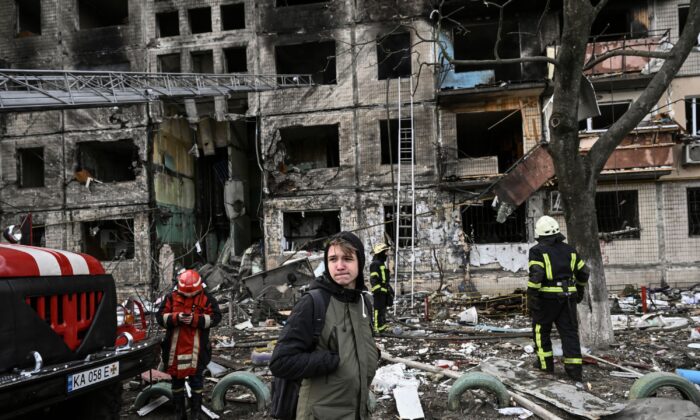 A citizen stands near firefighters in front of a destroyed apartment building after it was shelled in the northwestern Obolon district of Kyiv, Ukraine, on March 14, 2022. (Aris Messinis/AFP via Getty Images)