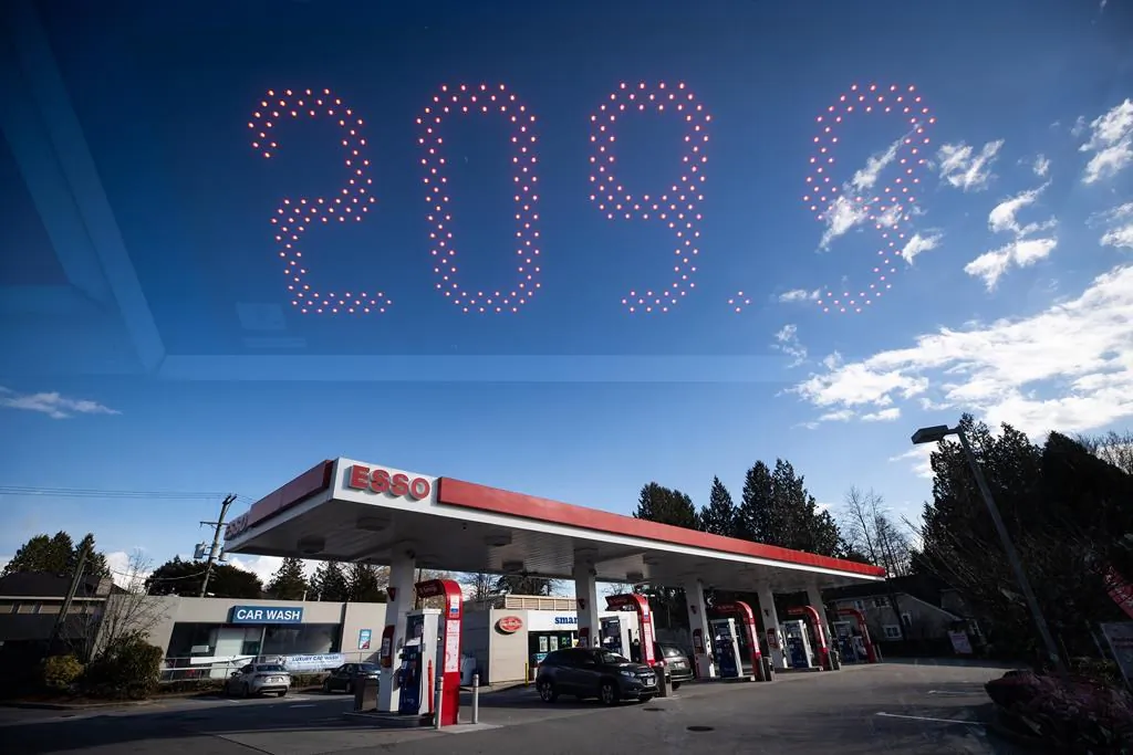 In this double exposure photograph, a sign displays the price of a litre of regular grade gasoline as people fuel up their vehicles at an Esso gas station, in Vancouver, on March 8, 2022. (The Canadian Press/Darryl Dyck)