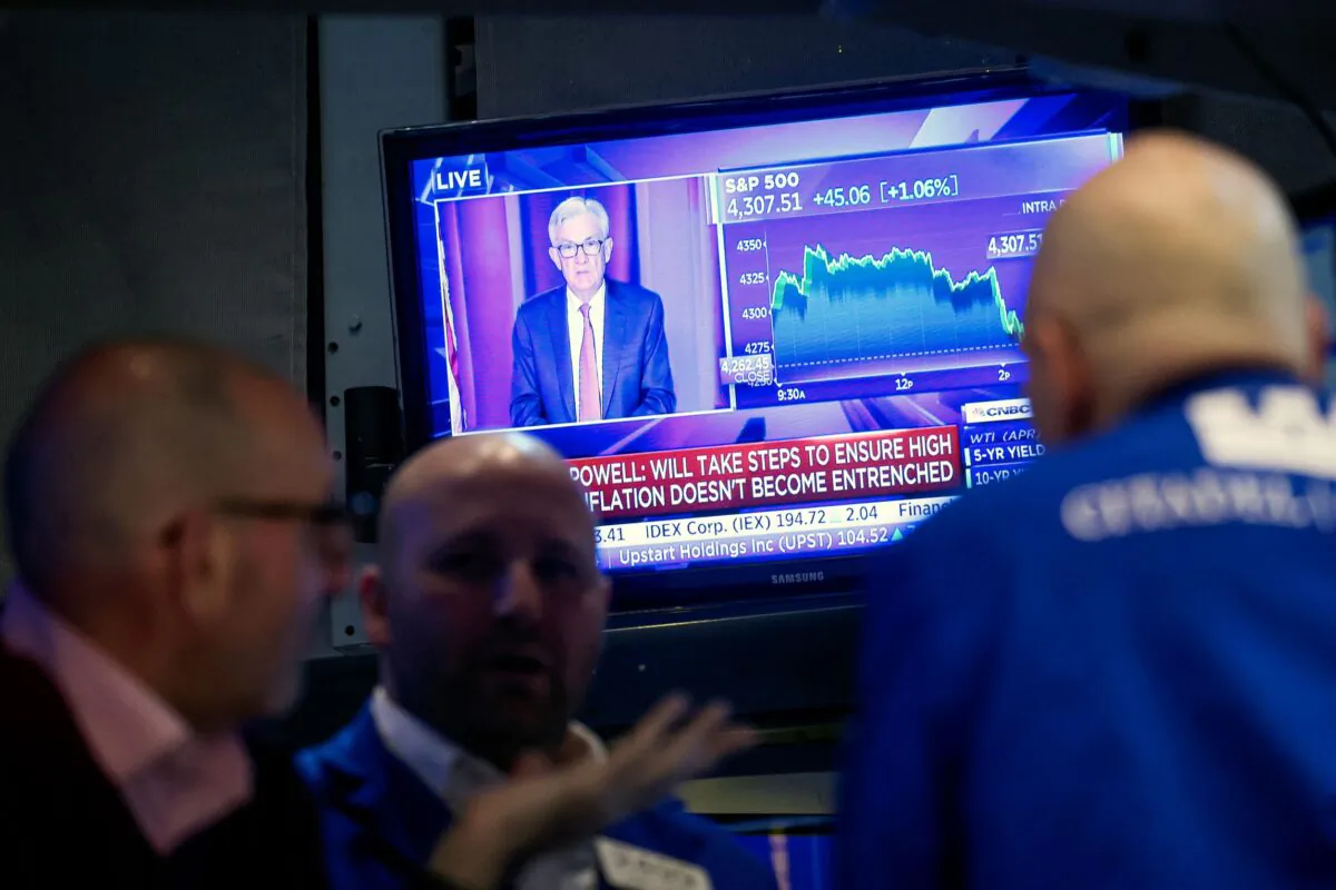 Traders work as Federal Reserve Chair Jerome Powell is seen on a screen delivering remarks at the New York Stock Exchange on March 16, 2022. (Brendan McDermid/Reuters)