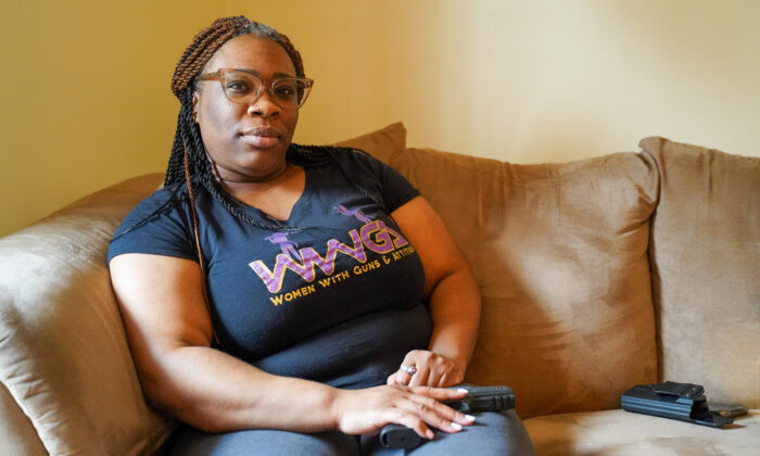 Jessica Luckett, dressed in a Women with Guns and Attitudes club T-shirt, sits on her living room couch with her gun in hand in Chicago, IL on Feb. 23, 2022. (Cara Ding/The Epoch Times)