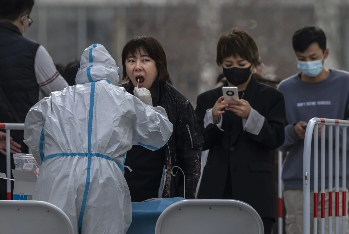 A medical worker wears protective clothing as she gives a woman a nucleic acid test at a mass testing site to prevent the spread of COVID-19 in Beijing, China, on March 15, 2022. (Kevin Frayer/Getty Images)