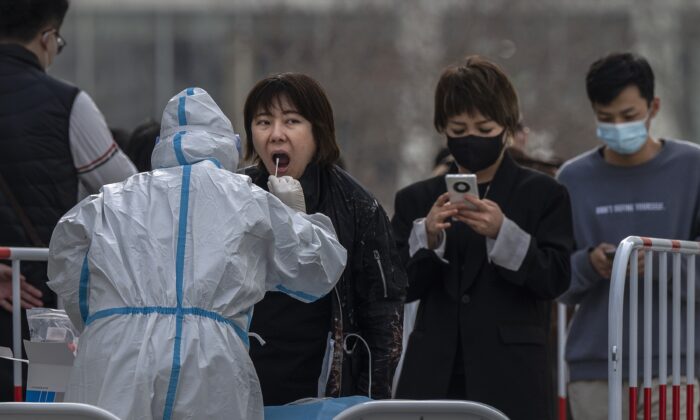 A medical worker wears protective clothing as she gives a woman a nucleic acid test at a mass testing site to prevent the spread of COVID-19 in Beijing, China, on March 15, 2022. (Kevin Frayer/Getty Images)