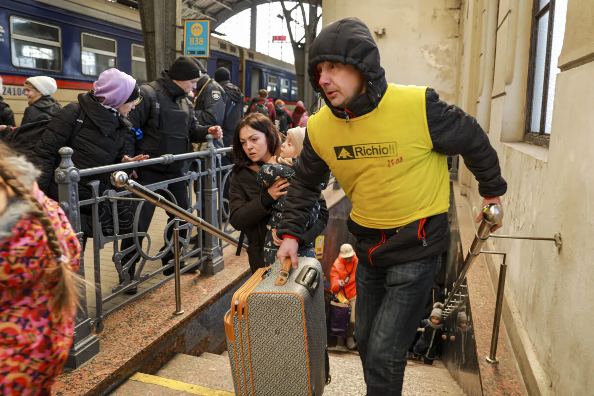 A volunteers helps carry luggage for Ukrainian refugees as they prepare to board a train to Poland at the train station in Lviv, Ukraine, on March 18, 2022. (Charlotte Cuthbertson/The Epoch Times)