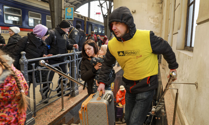 A volunteers helps carry luggage for Ukrainian refugees as they prepare to board a train to Poland at the train station in Lviv, Ukraine, on March 18, 2022. (Charlotte Cuthbertson/The Epoch Times)