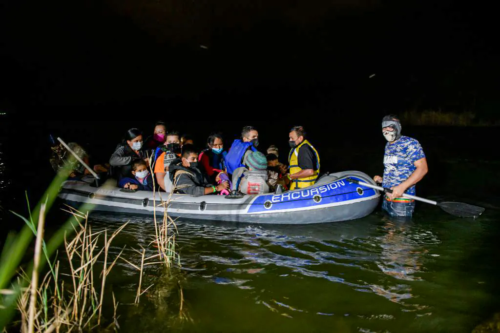 A coyote people smuggler (R) guides an inflatable boat carrying migrants from Central America arriving illegally from Mexico to the United States to seek asylum, on the Rio Grande river at the border city of Roma, Texas, on March 29, 2021. (Ed Jones/AFP via Getty Images)