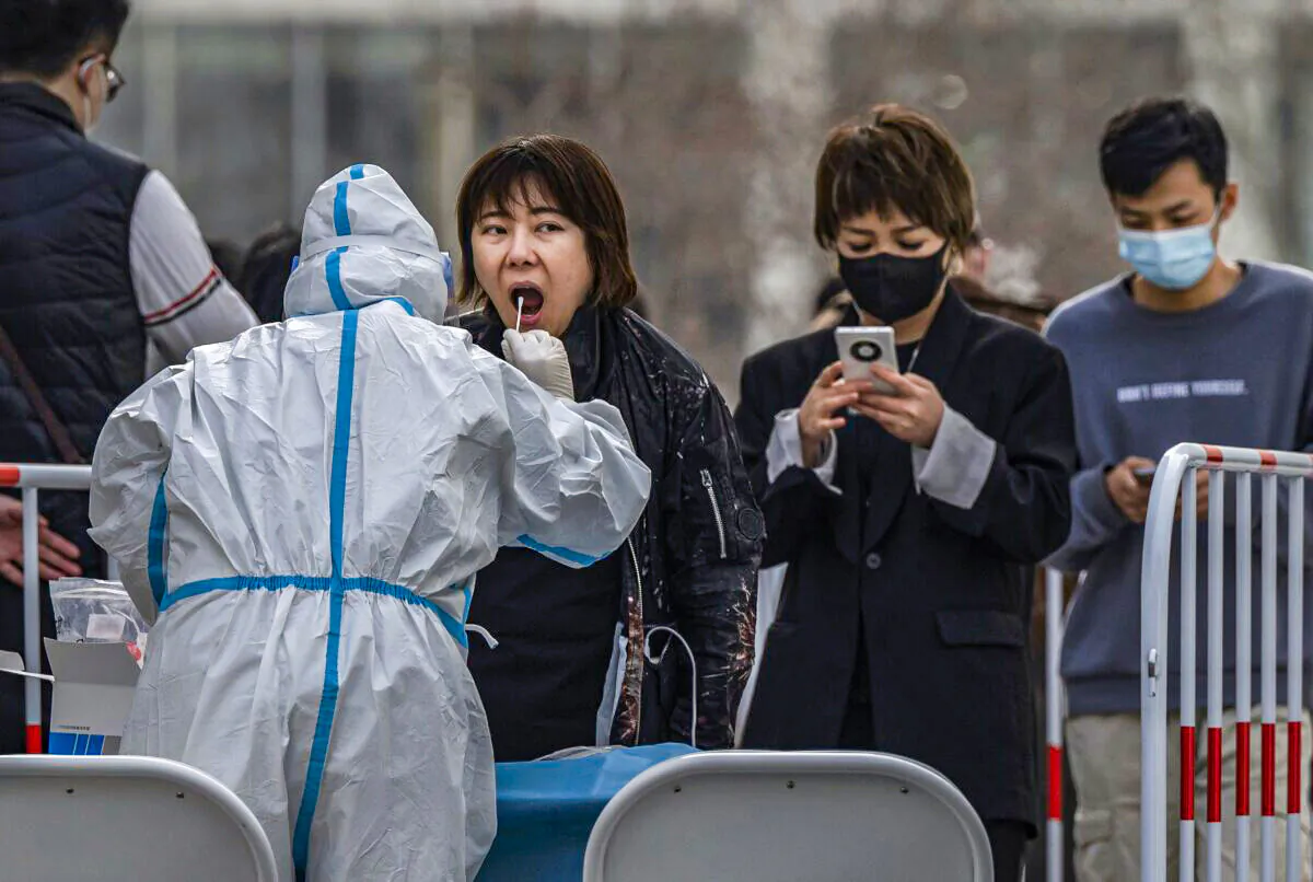A medical worker wears protective clothing as she gives a woman a nucleic acid test at a mass testing site to prevent the spread of COVID-19 in Beijing, China, on March 15, 2022. (Kevin Frayer/Getty Images)