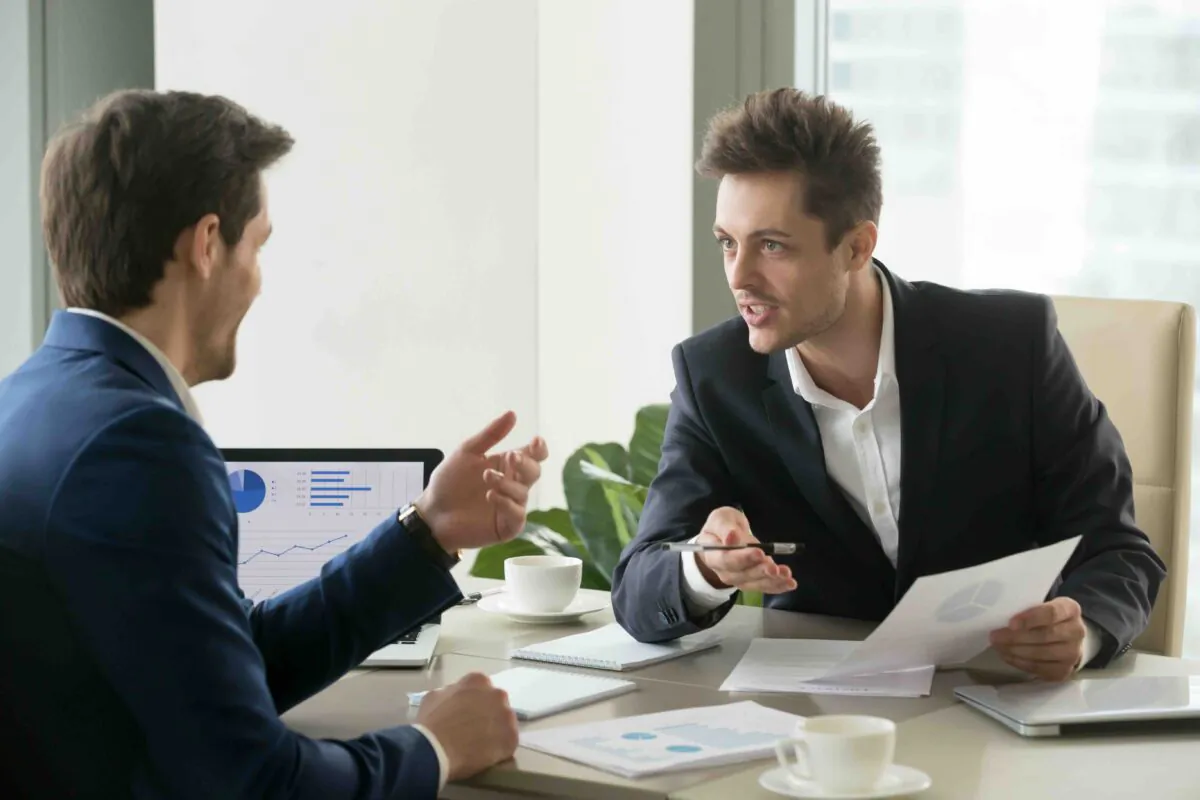Two successful businessmen discussing company financial strategy, analyzing economic indicators, planning profitability, and stock value growth while sitting in office during a business meeting. ((fizkes/Shutterstock)