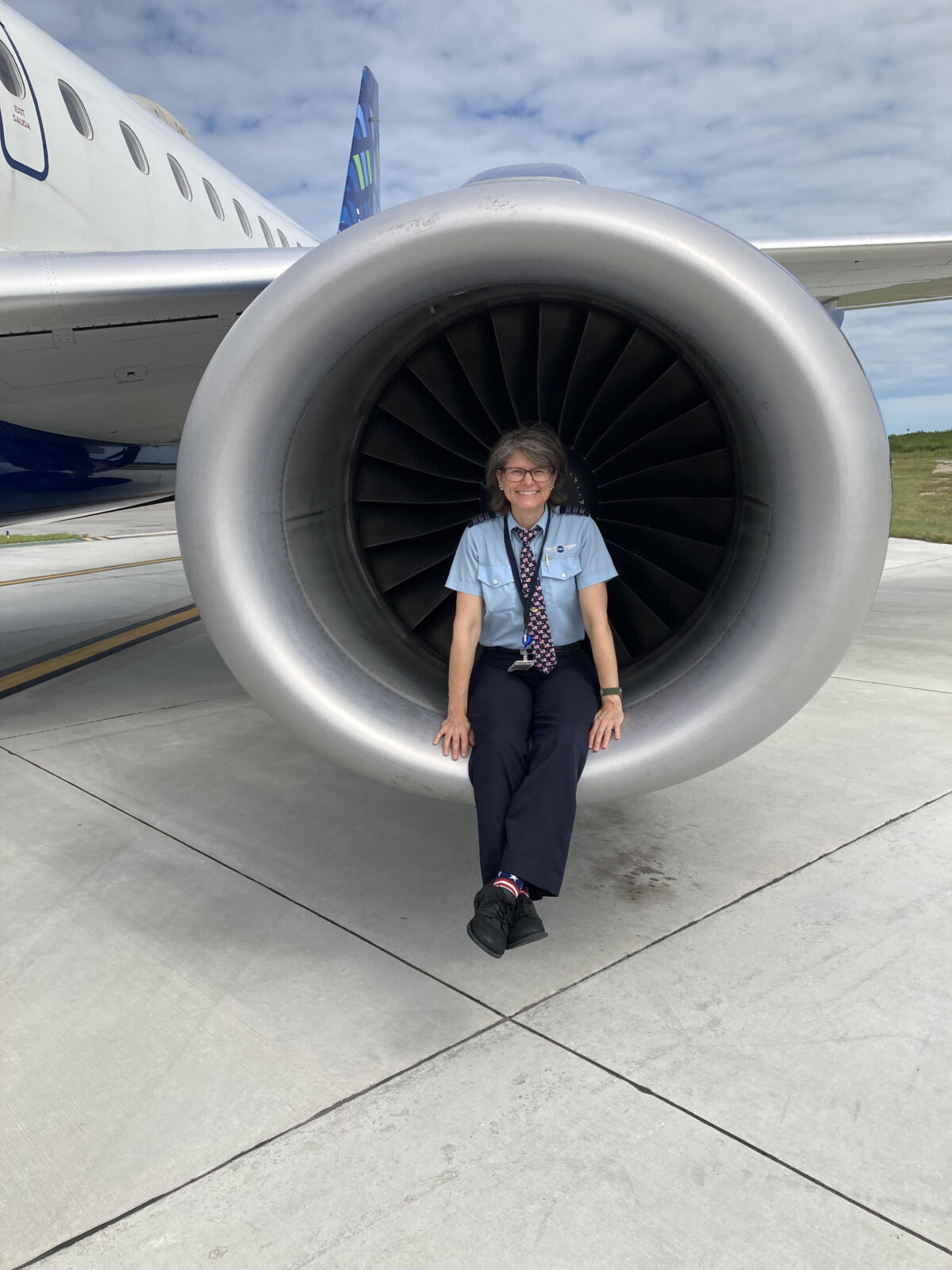 Jet Blue pilot, Janviere Carlin, sits on the edge of an engine turbine and the plane rests on the tarmac. 