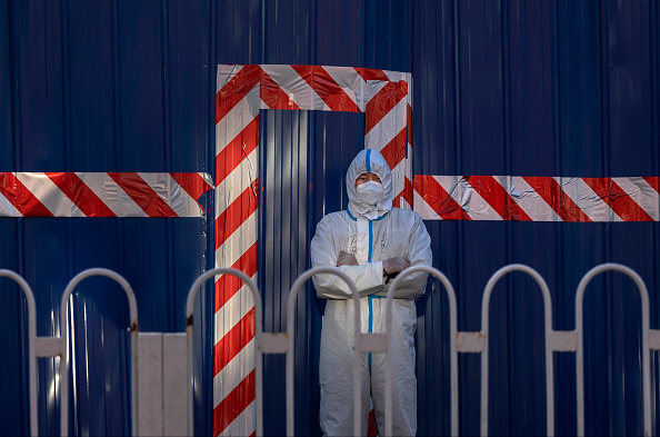 A guard wears a protective suit as he watches over a barricaded community that was locked down for health monitoring after recent cases of COVID-19 were found in the area on March 21, 2022 in Beijing, China.  (Photo by Kevin Frayer/Getty Images)