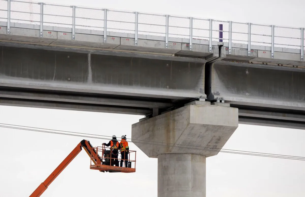 Workers are shown beneath a section of the Réseau express métropolitain, a new automated light rail network under construction in Montreal, on Feb. 2, 2022. (The Canadian Press/Graham Hughes)