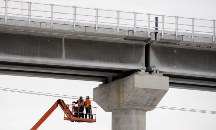 Workers are shown beneath a section of the Réseau express métropolitain, a new automated light rail network under construction in Montreal, on Feb. 2, 2022. (The Canadian Press/Graham Hughes)