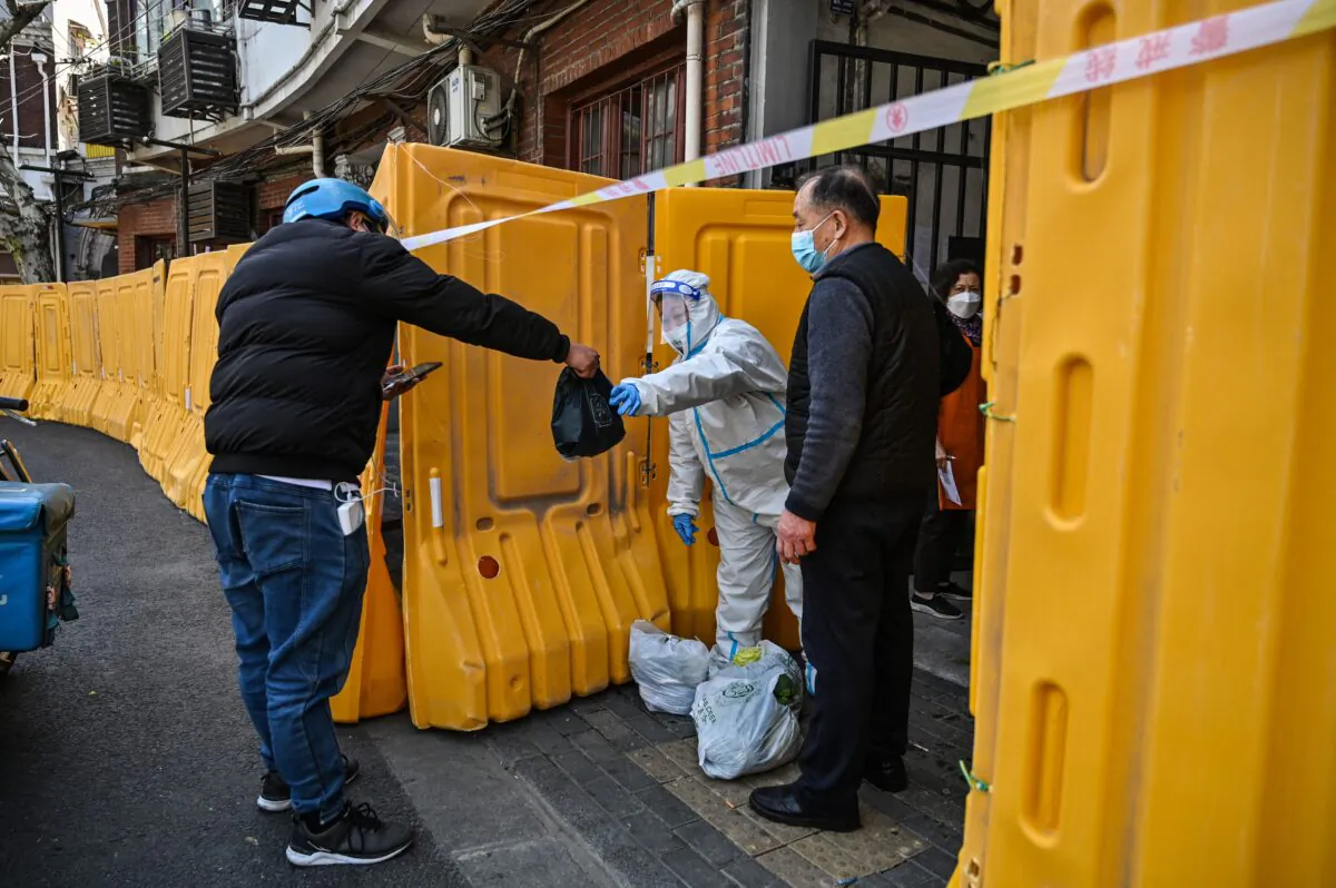A worker, wearing a protective gear, guards the entrance to a neighborhood in lockdown as a measure against the Covid-19 coronavirus receive food from a delivery man, in Jing'an district, in Shanghai on March 29, 2022. (Hector Retamal/AFP via Getty Images)