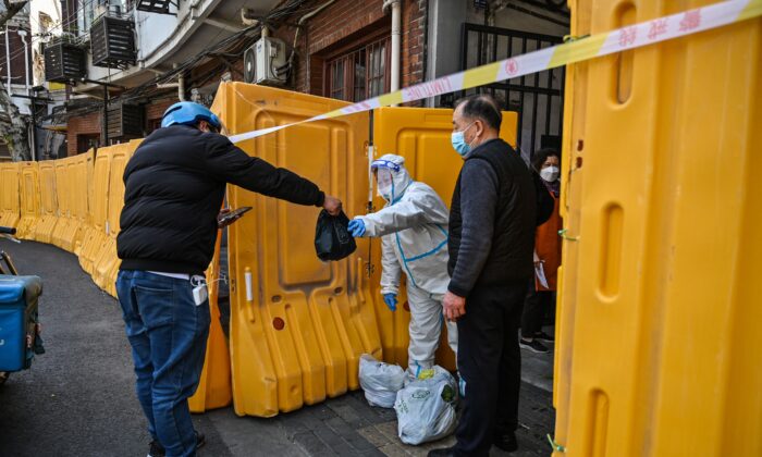 A worker, wearing a protective gear, guards the entrance to a neighborhood in lockdown as a measure against the Covid-19 coronavirus receive food from a delivery man, in Jing'an district, in Shanghai on March 29, 2022. (Hector Retamal/AFP via Getty Images)