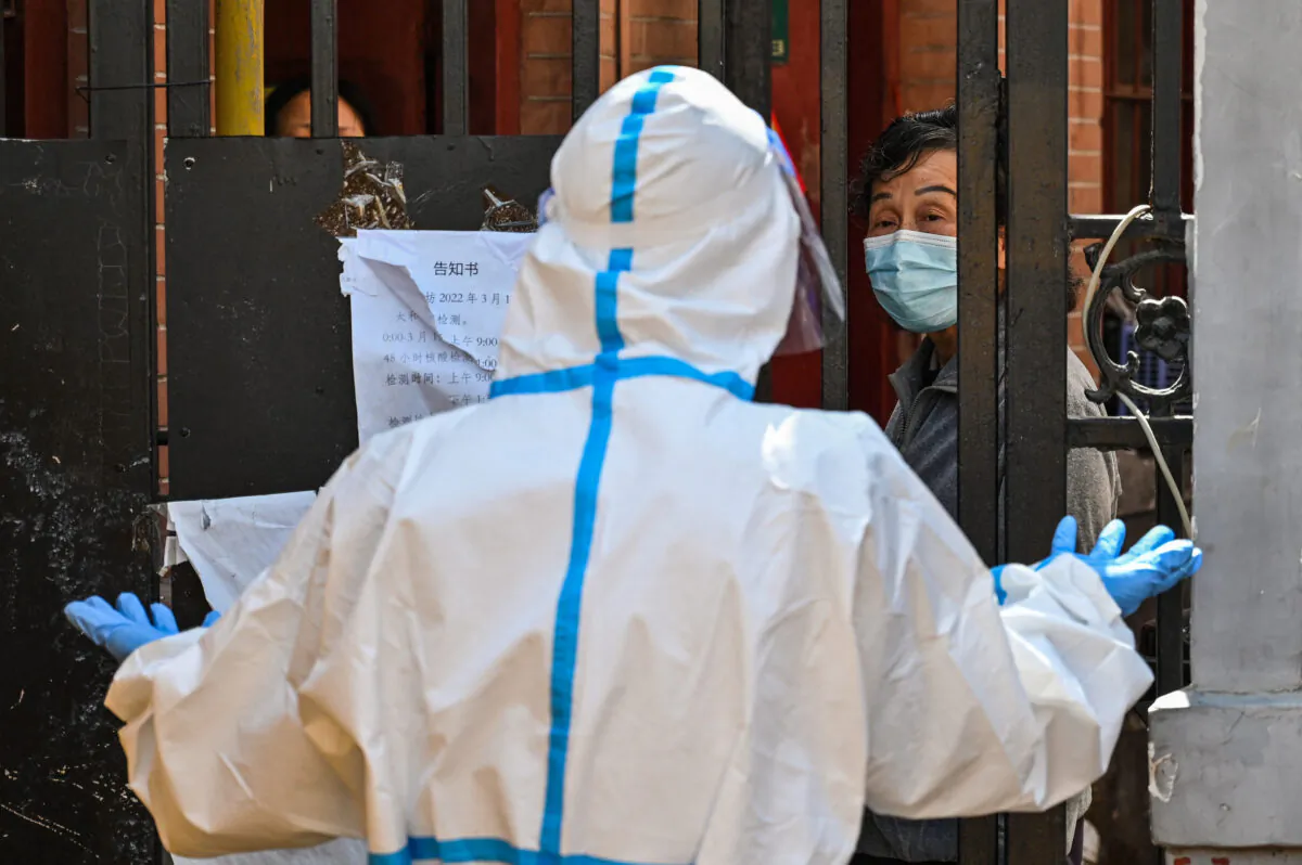 A worker, wearing protective gear, guards the entrance to a neighbourhood in lockdown in Jing'an district, Shanghai on March 29, 2022. (Hector Retamal/AFP via Getty Images)