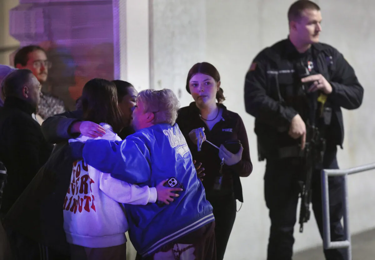 People embrace after being reunited as a police officer stands by following a shooting at Fashion Outlets of Chicago mall in Rosemont, Ill., on March 25, 2020. (Chris Sweda/Chicago Tribune/TNS)