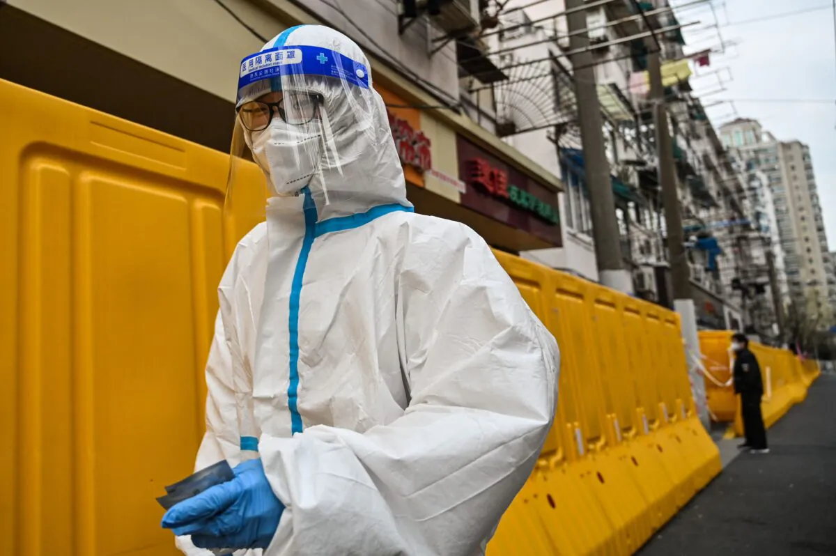 A worker wearing a protective gear walks next to barriers that separate from the street a neighborhood in lockdown as a measure against COVID-19 in Jing'an district, Shanghai, on March 30, 2022. (Hector Retamal/AFP via Getty Images)