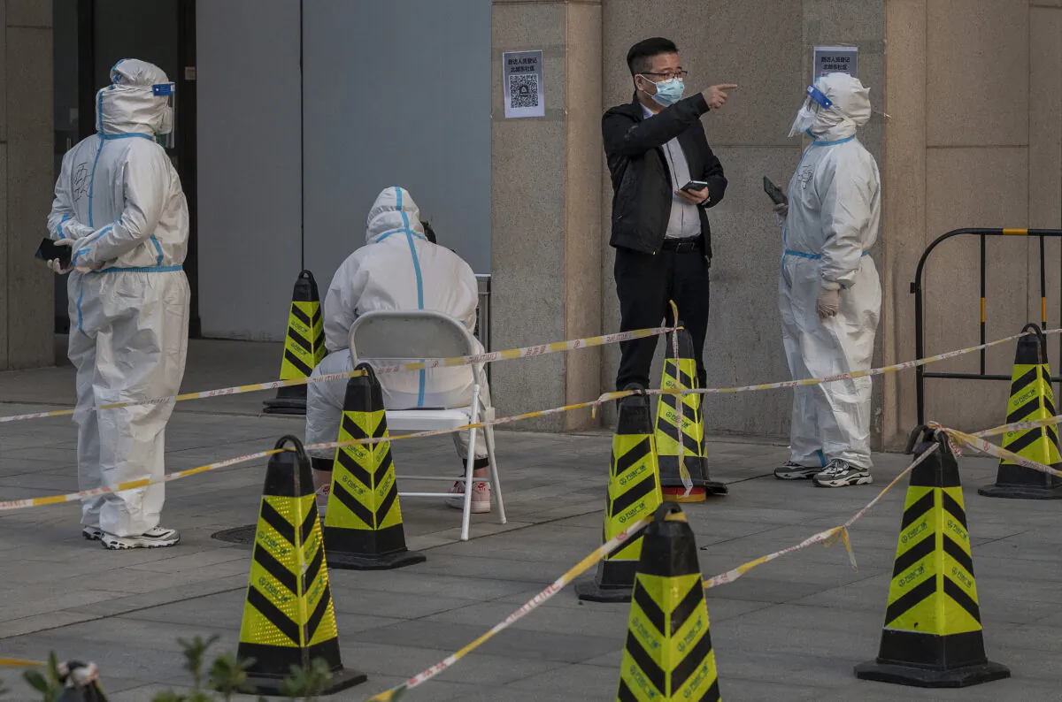 A man talks to health workers dressed in protective clothing as he asks a question at a mass COVID-19 testing site at an office building in Beijing on March 14, 2022. (Kevin Frayer/Getty Images)