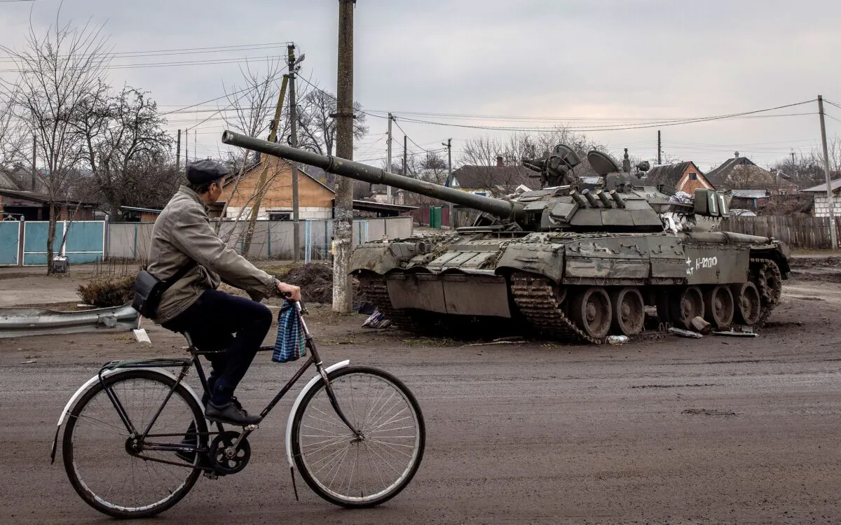 A man rides his bike past a destroyed Russian tank in Trostyanets, Ukraine, on March 30, 2022. (Chris McGrath/Getty Images)